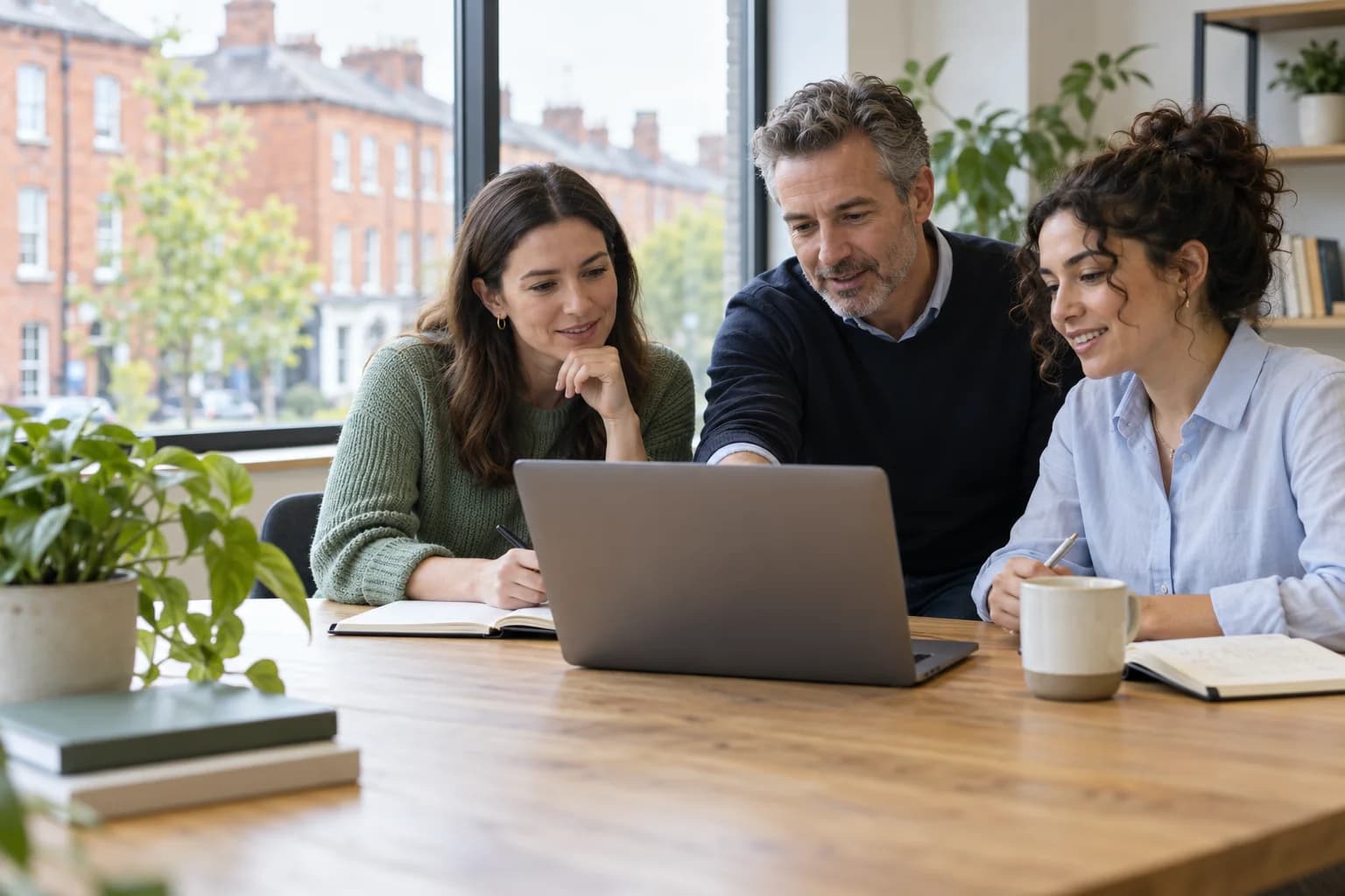 Illustrative scene of three colleagues learning together around a laptop in a bright Dublin office.
